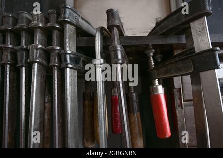 Screw clamps hanging in a row in the workshop of a craftsman, copy space, selected focus, narrow depth of field Stock Photo
