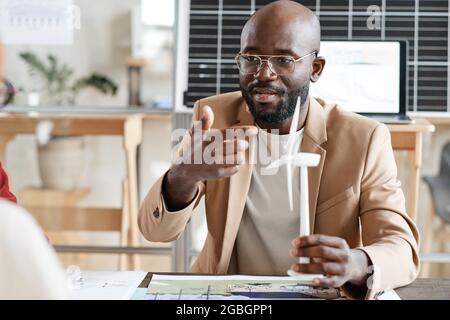African architect pointing at model of windmill in his hand and presenting it to his colleagues Stock Photo