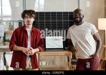 Portrait of two young designers smiling at camera while standing between the laptop with online presentation on the screen Stock Photo