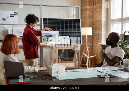 Young architect holding project of new building and presenting it to his colleagues during meeting at office Stock Photo