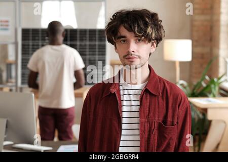 Portrait of young designer looking at camera while working at office with his colleagues Stock Photo