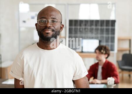 Portrait of African confident businessman in white T-shirt looking at camera while working at office with his colleagues Stock Photo