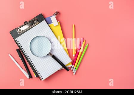 Notebooks, pens, a magnifying glass on a pink background. School supplies. Stock Photo