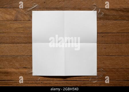 White paper folded in four fraction stuck on the wooden board by adhesive tape Stock Photo