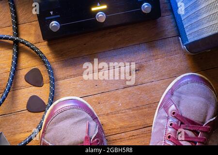 Guitarist's point of view on the stage floor. Guitar pedal, cable, guitar pick, amplifier and shoes on wooden floor. Stock Photo
