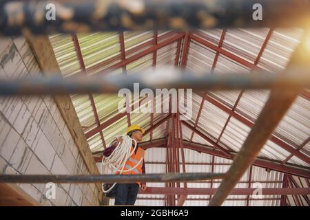 Low angle view of a construction worker standing on a building site carrying plastic pipe Stock Photo