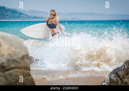 Woman walking out of the sea carrying her surfboard, Punta Paloma beach, Tarifa, Cadiz, Andalucia, Spain Stock Photo