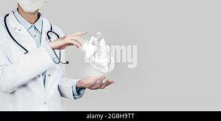 Female doctor holding virtual volumetric drawing of Heart in hand. Handrawn human organ, copy space on right side, grey hdr color. Healthcare hospital Stock Photo