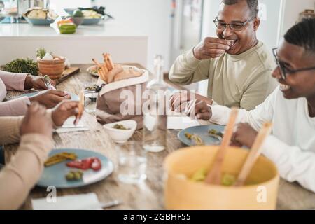 Happy black family eating lunch sitting at dinner table at home - Focus on fathers face Stock Photo