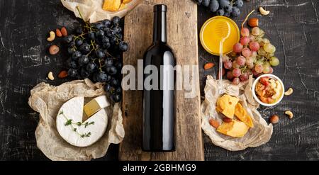 Wine and cheese composition. Red wine bottle mockup on vintage cutting wooden board. Gastronomy Ingredients different cheese grapes honey. Red wine Stock Photo