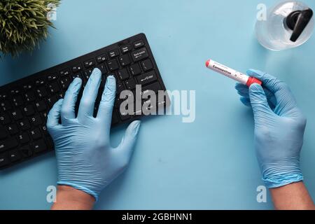 hand in blue medical gloves holding blood test tube and typing on keybaord Stock Photo