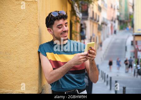 Young caucasian man with false nails using the phone standing against a wall. Stock Photo
