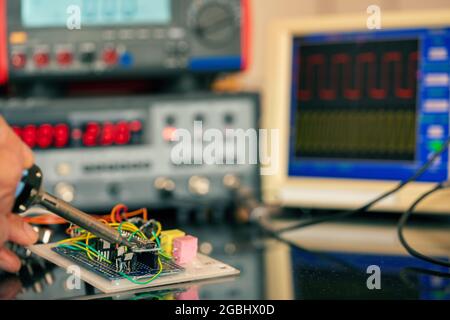 Manufacturing and setting up an electronic device in the laboratory. Soldering iron and electronic measuring instruments Stock Photo