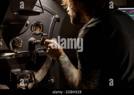 Bearded man using coffee roasting machine at factory Stock Photo