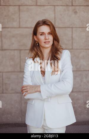 Business woman in white suit posing with crossing arms. Confident stylishly dressed woman Stock Photo