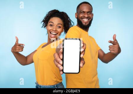 Cheerful black couple pointing at smartphone with mockup on screen, recommending mobile app, advertising your website Stock Photo