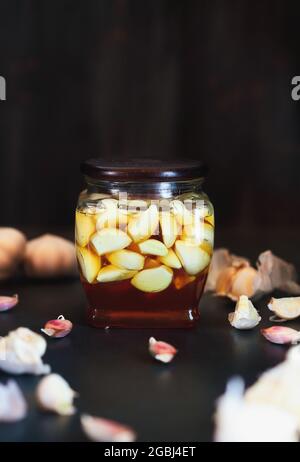 Fermented garlic cloves in a jar of honey, a rich source of  probiotics, over a rustic wood background table. Selective focus with blurred background Stock Photo