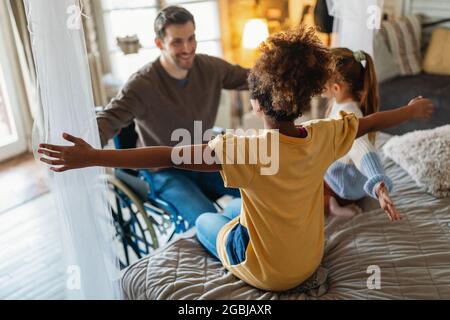 Portrait of happy loving father with disability in wheelchair hugging with multiethnic children Stock Photo