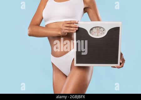 Woman Holding Bathroom Scales Isolated On Blue Studio Wall Stock Photo