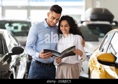 Loving arab couple checking booklet in car salon Stock Photo