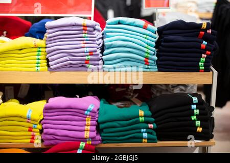 There are stacks of knitted sweaters, folded longsleeves or T-shirts on a store shelf. Selling clothes in a store. Stock Photo