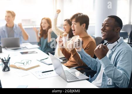 Group of excited people using laptop and shaking clenched fists Stock Photo