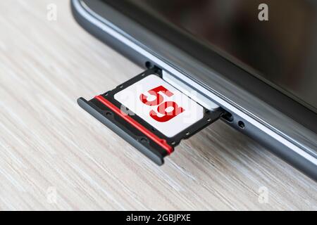 Broadband 5G mobile communication technology concept : SIM card tray, dual SIM card slot with two nano SIM cards on wooden background. Stock Photo