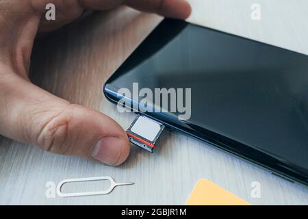 SIM card and microSD card tray with removal tool at the side of smartphone on a wooden table. free space for design and text Stock Photo