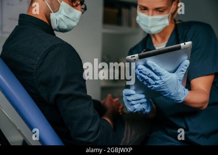 Mixed race male patient chatting to female nurse holding digital tablet Stock Photo