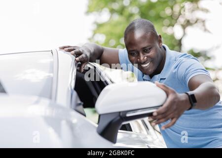 Excited black man standing by white car, looking at mirror Stock Photo