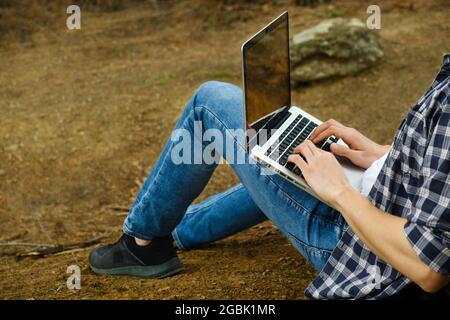 Man sitting on ground at forest and working on laptop Stock Photo