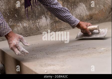 Indian labour levelling plastered floor using flat trowel and cement manually, Stock image. Stock Photo