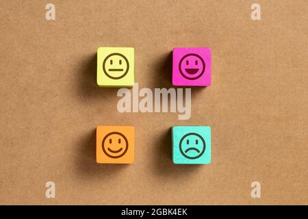 Emoticon faces in colors wooden blocks over brown wood paper. Service evaluation and satisfaction survey concepts. Angry, neutral, good mood and happy Stock Photo