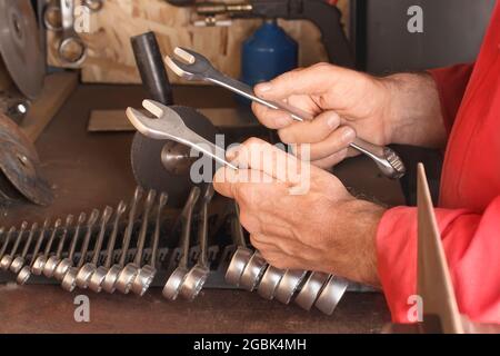 Master holds in his hands two spanners of a set of keys on a work bench with tools in the garage Stock Photo