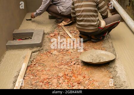 Indian construction workers plastering floor using trowel and cement manually, Stock image. Stock Photo