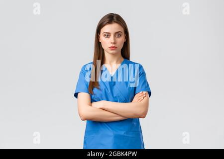 Healthcare workers, prevent virus, insurance and medicine concept. Serious and confident female nurse in blue scrubs, intern or physician cross arms Stock Photo