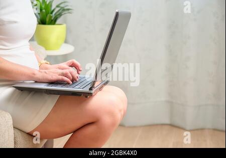 young caucasian woman working from home with her laptop on top of her legs sitting on the sofa Stock Photo