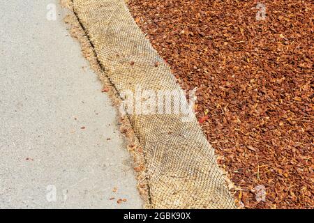 Straw wattle separate ground covered with mulch and asphalt walkway to reduce debris runoff during landscaping, construction and maintenance project. Stock Photo