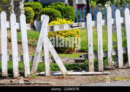 Broken fence. Damaged weathered white picket fence with broken rails and planks in residential neighborhood Stock Photo