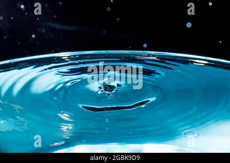 Water drop on blue background. Blue water surface with splash. Clear Waterdrop with circular waves. Splashes closeup. Water splash and falling drop. S Stock Photo