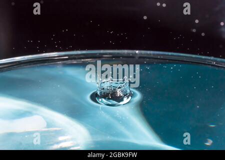 Water splash in crown shape and falling drop. Splash of the falling drops of water. Water drop on blue background. Blue water surface with splash. Cle Stock Photo