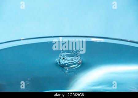 Water splash in crown shape and falling drop. Splash of the falling drops of water. Water drop on blue background. Blue water surface with splash. Cle Stock Photo
