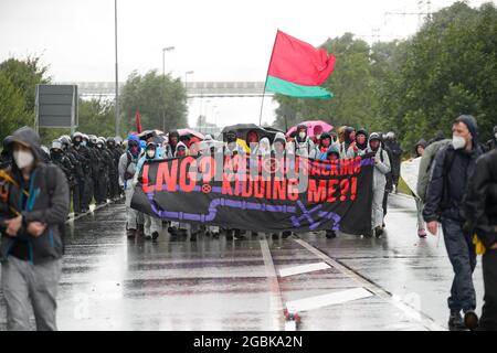 31 July 2021, Schleswig-Holstein, Brunsbüttel: Activists, accompanied by police, walk through ChemCoastPark with a placard reading 'LNG? Are you fracking kidding me?!' through ChemCoastPark. During a demonstration against a planned terminal for liquefied natural gas (LNG), activists of the alliance 'Ende Gelände' occupied several tracks in an industrial area. Photo: Jonas Walzberg/dpa Stock Photo