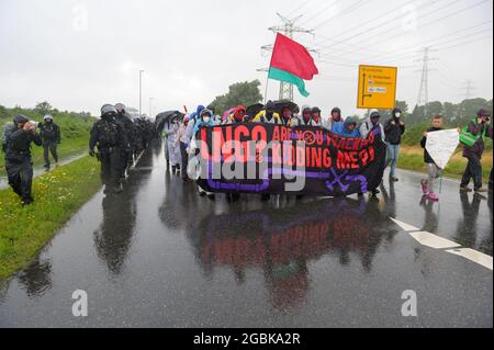 31 July 2021, Schleswig-Holstein, Brunsbüttel: Activists, accompanied by police, walk through ChemCoastPark with a placard reading 'LNG? Are you fracking kidding me?!' through ChemCoastPark. During a demonstration against a planned terminal for liquefied natural gas (LNG), activists of the alliance 'Ende Gelände' occupied several tracks in an industrial area. Photo: Jonas Walzberg/dpa Stock Photo