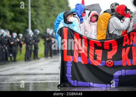 31 July 2021, Schleswig-Holstein, Brunsbüttel: Police officers stand next to a protest with a placard that reads 'LNG? Are you fracking kidding me?!' at ChemCoastPark. During a demonstration against a planned terminal for liquefied natural gas (LNG), activists of the alliance 'Ende Gelände' occupied several tracks in an industrial area. Photo: Jonas Walzberg/dpa Stock Photo