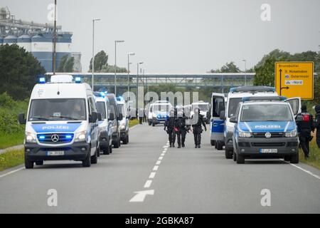 31 July 2021, Schleswig-Holstein, Brunsbüttel: Police officers walk in front of a demonstration in the ChemCoastPark industrial area. During a demonstration against a planned terminal for liquefied natural gas (LNG), activists of the alliance 'Ende Gelände' occupied several tracks in an industrial area. Photo: Jonas Walzberg/dpa Stock Photo