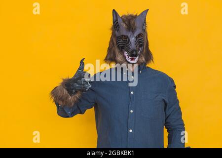 On a yellow background there is a werewolf dressed in a blue shirt is making a appointment gesture with thumbs-up. Stock Photo