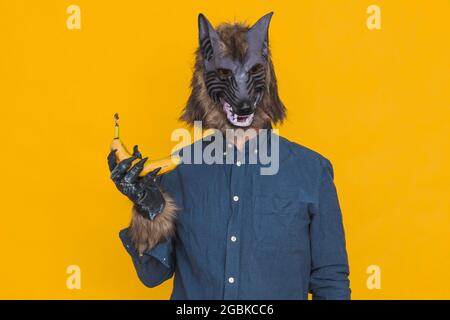 On a yellow background there is a werewolf dressed in a blue shirt holding an unpeeled banana in his right hand. Stock Photo