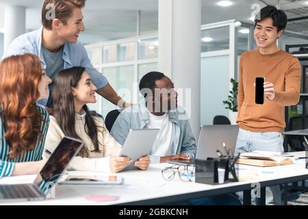 Diverse group of students sitting at desk guy showing phone Stock Photo