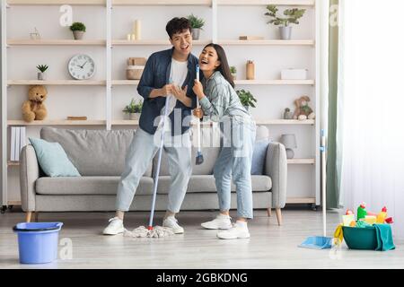 Funny asian couple singing songs while cleaning apartment, copy space Stock Photo